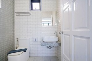 Un baño con paredes de azulejos blancos, un inodoro, un lavabo y una puerta.