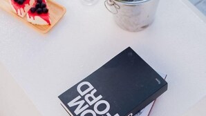 A book titled "DOPING" on a white table with a wine bottle in a metal container and a slice of cake with berries.