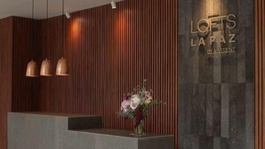 A reception desk with a modern design, featuring a wooden panel wall and a dark textured backdrop. - Lofts La Paz (Guadalajara)