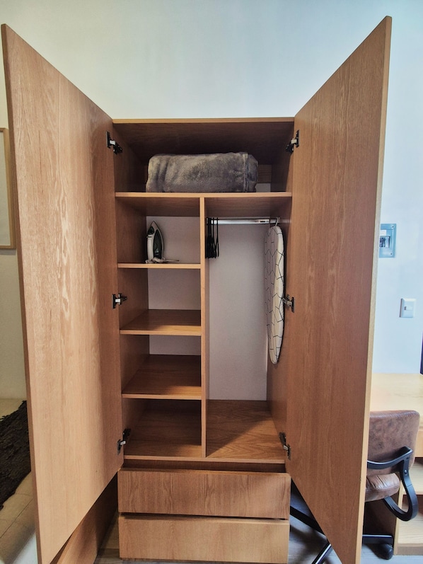 Un armario de madera con varios estantes, una barra para colgar ropa y una toalla doblada encima.