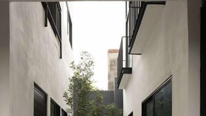 A narrow, covered walkway with potted plants and a tree, flanked by white walls and black railings. - Lofts La Paz (Guadalajara)