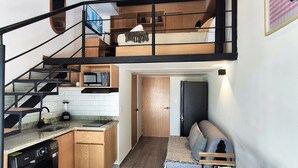 A compact kitchen with a washing machine, a dining area with a table and benches, a loft bedroom with a bunk bed, and a staircase. - Lofts La Paz (Guadalajara)