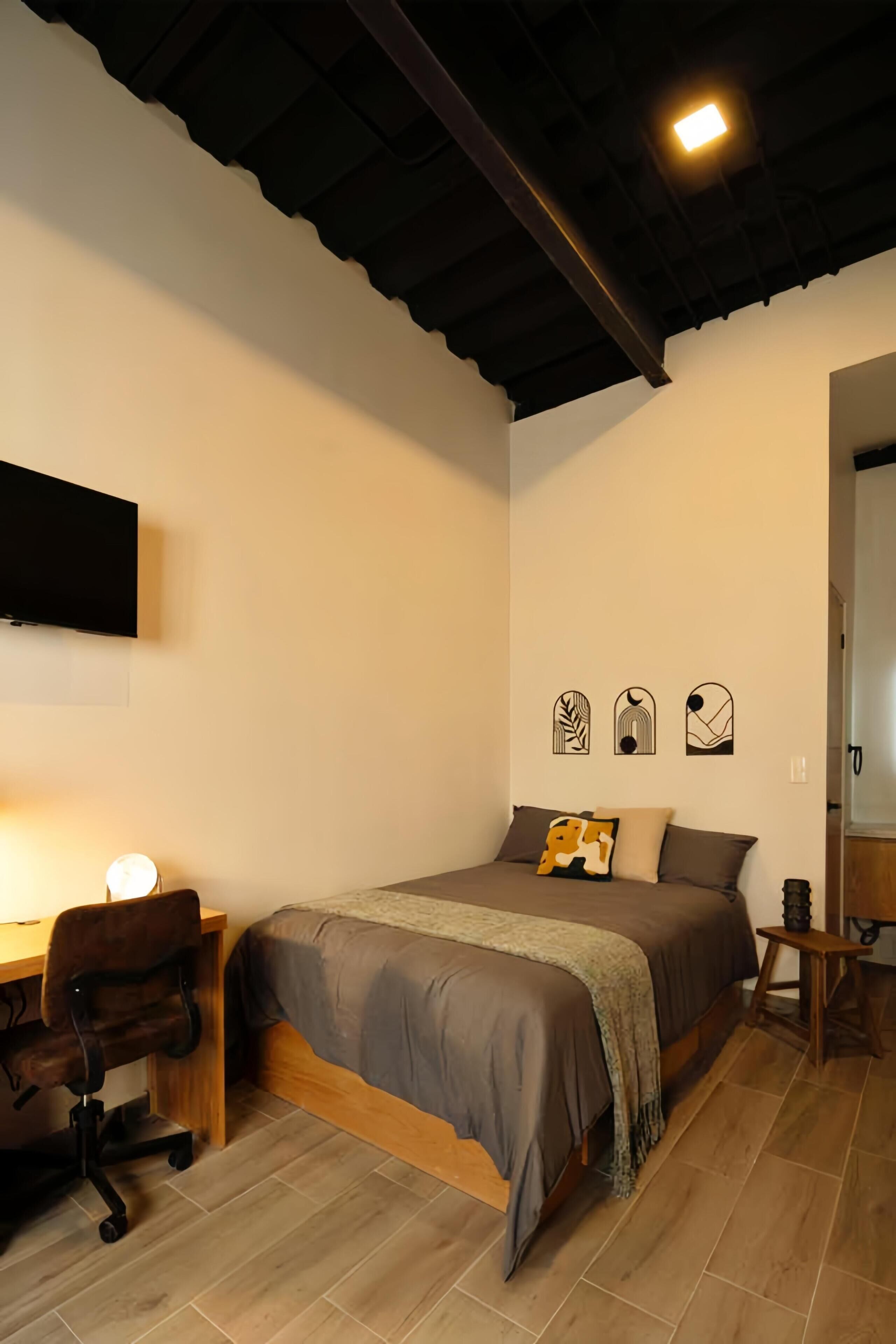 Une chambre à coucher comprenant un lit, un bureau, une chaise et un téléviseur fixé au mur.