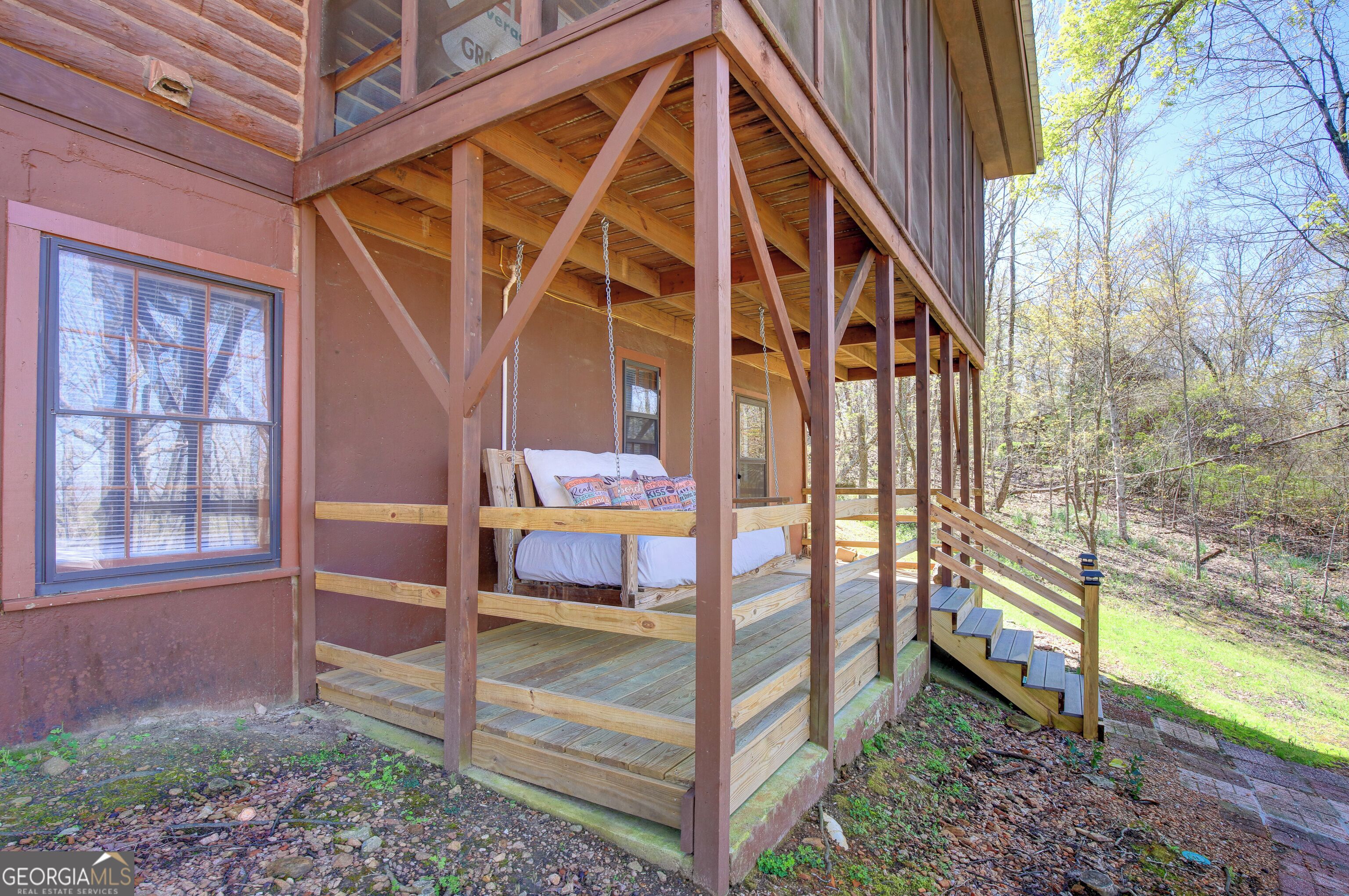 A wooden cabin with a porch, a bed with pillows, and a staircase leading to the porch.