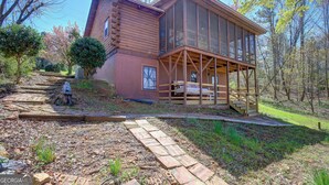 A log cabin with a large glass extension, a wooden deck, and a stone pathway leading to the entrance.