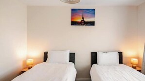 Une chambre d’hôtel avec deux lits, un tableau représentant la Tour Eiffel et des lampes de chevet.
