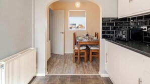 Une cuisine avec des meubles blancs, un plan de travail noir et un coin repas comprenant une table et des chaises.