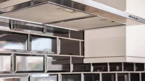 Une cuisine avec un dosseret de carreaux noirs, des casseroles en acier inoxydable sur la cuisinière et un porte-ustensiles contenant des cuillères en bois.