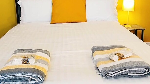 Ein Hotelzimmer mit Bett, gelber Wand, einem Löwenbild und einem Nachttisch mit Lampe.