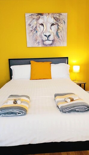 Una camera d'albergo con un letto, una parete gialla, un quadro di un leone e un comodino con una lampada.