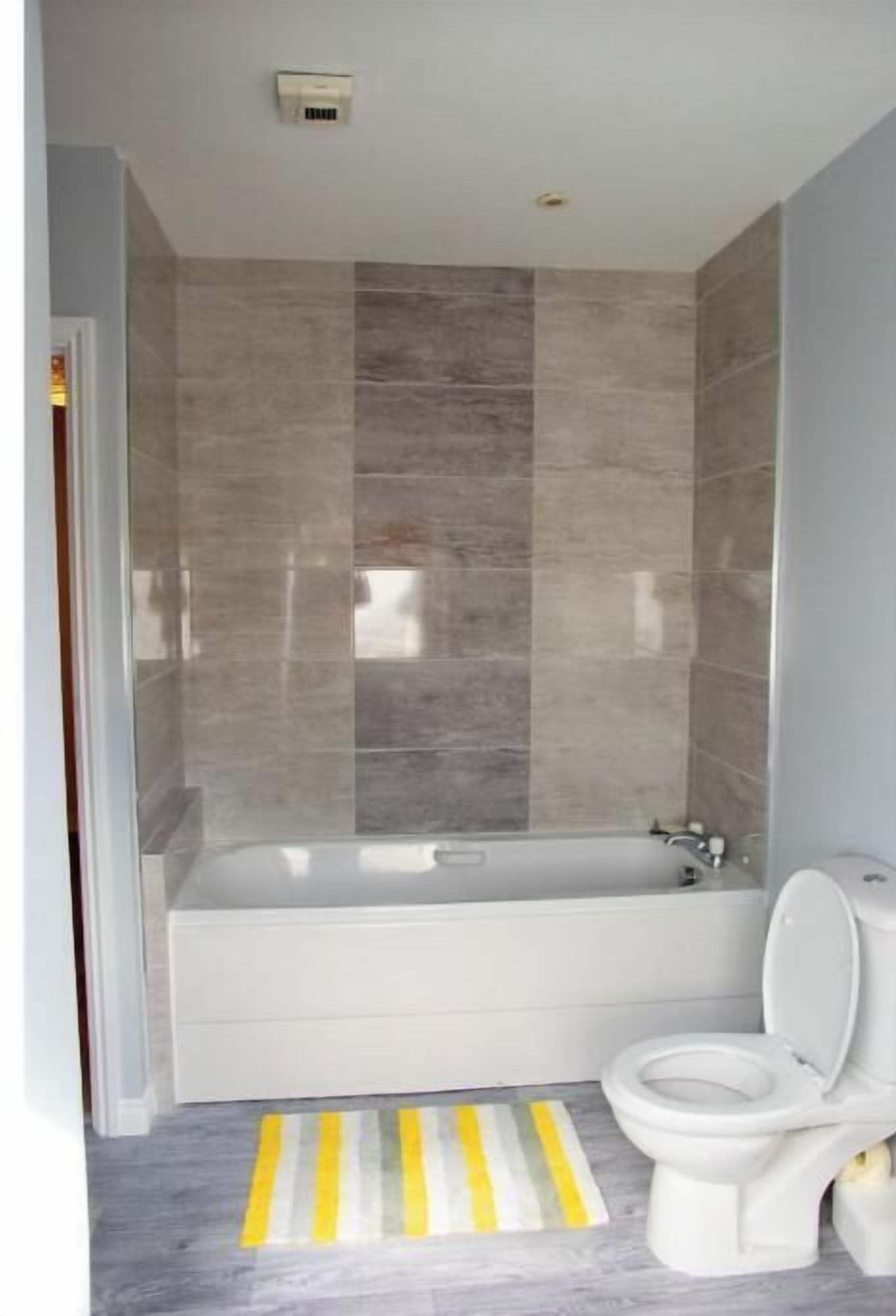 A modern bathroom with a bathtub, toilet, and a striped rug on the floor.