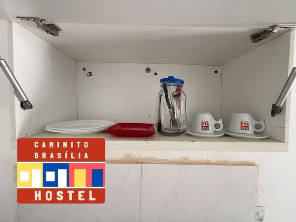 A kitchenette with a jar, plates, and cups on the counter.