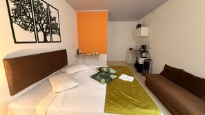 A hotel room with a bed, a sofa, a small kitchenette, and a wall with a framed picture. - Caminito Brasilia Hotel (Luziânia)