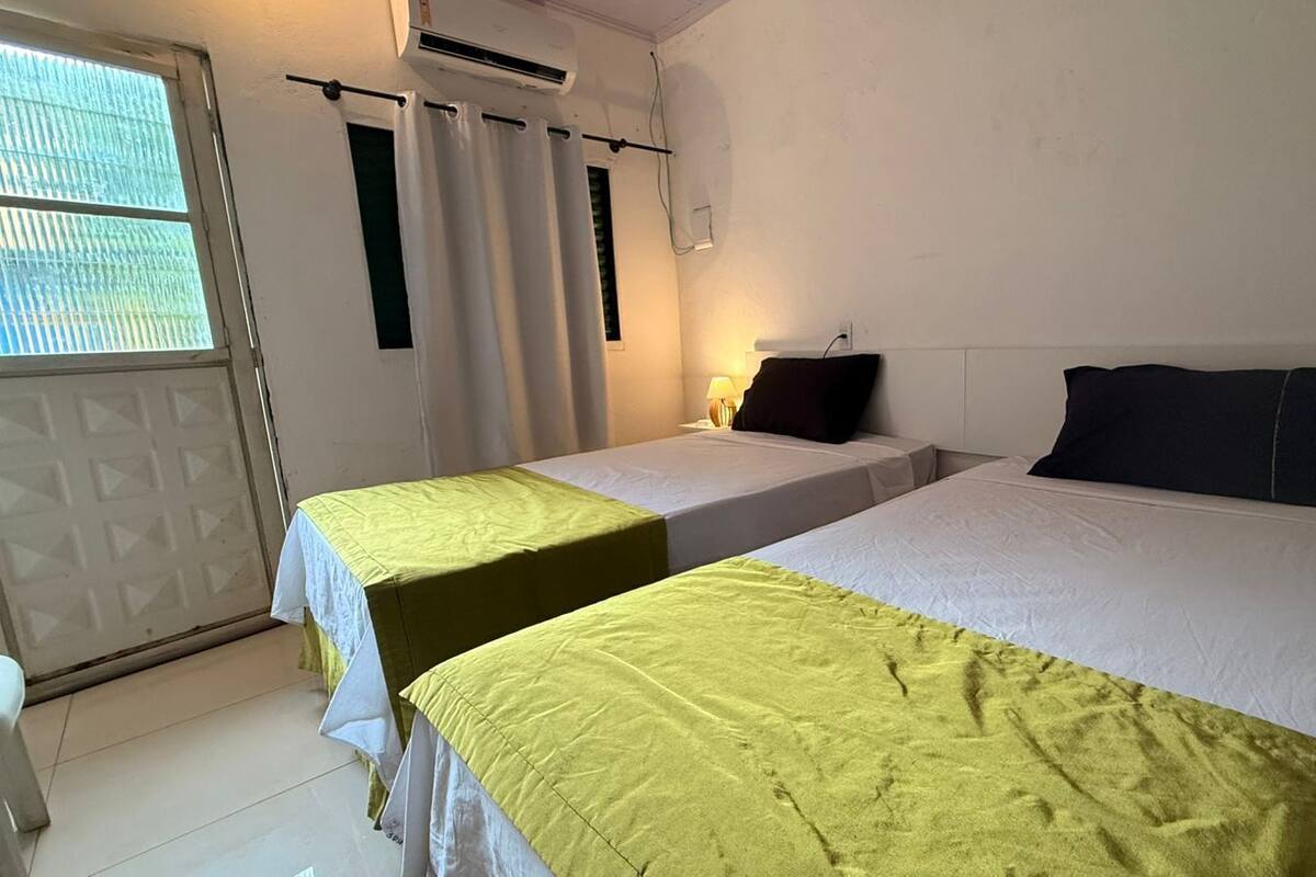 Habitación de hotel con dos camas, una ventana con cortinas, un equipo de aire acondicionado y una lámpara.