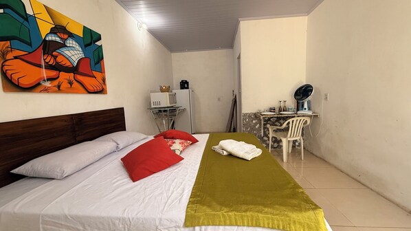 A room with a bed, a desk, a chair, a fan, and a microwave. - Caminito Brasilia Hotel (Luziânia)
