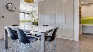 A modern dining area with a white table and black chairs, a clock on the wall, and a kitchen in the background. - Spacious 2-bed Apartment Close to City (Sydney)