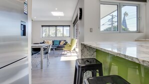 A modern kitchen with a marble countertop, a dining area with a sofa and chairs, and a view of the outside through large windows. - Spacious 2-bed Apartment Close to City (Sydney)