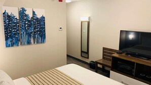 A hotel room with a bed, a flat-screen TV, a painting of trees, a mirror, and a small table with a microwave. - Chandni Victoria Hotel (Mississauga)