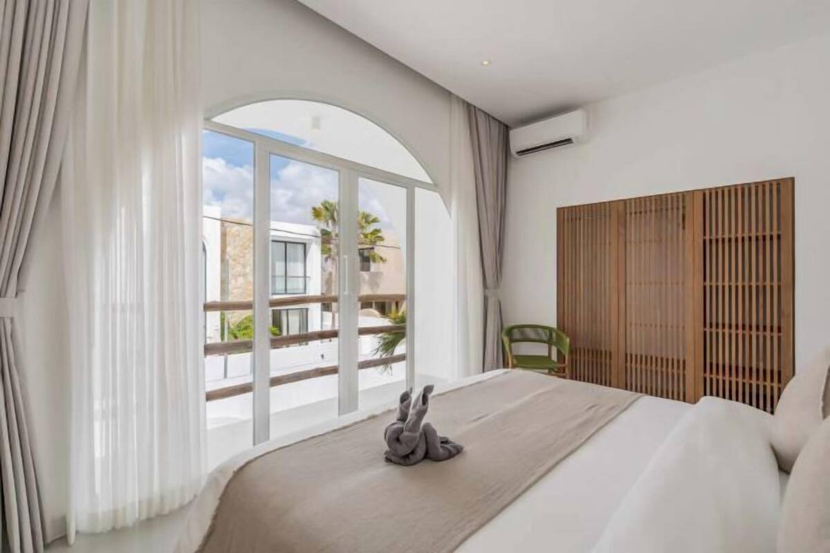 A hotel room with a large window, a bed, a green chair, and a wooden partition.