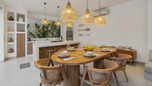 A modern kitchen with a central island, pendant lighting, and wicker chairs around a wooden dining table. - Villa Las Casas 2 by BaliSuperHost (Bali)