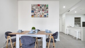 A modern dining area with a white table, grey upholstered chairs, and a collage of travel photos on the wall. - The Skyline Stopover - Near Sydney Airport (Mascot)