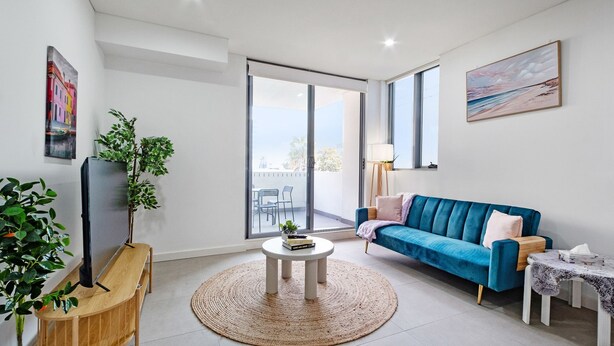 A modern living room with a blue sofa, a round coffee table, and a TV on a wooden stand. - The Skyline Stopover - Near Sydney Airport (Mascot)