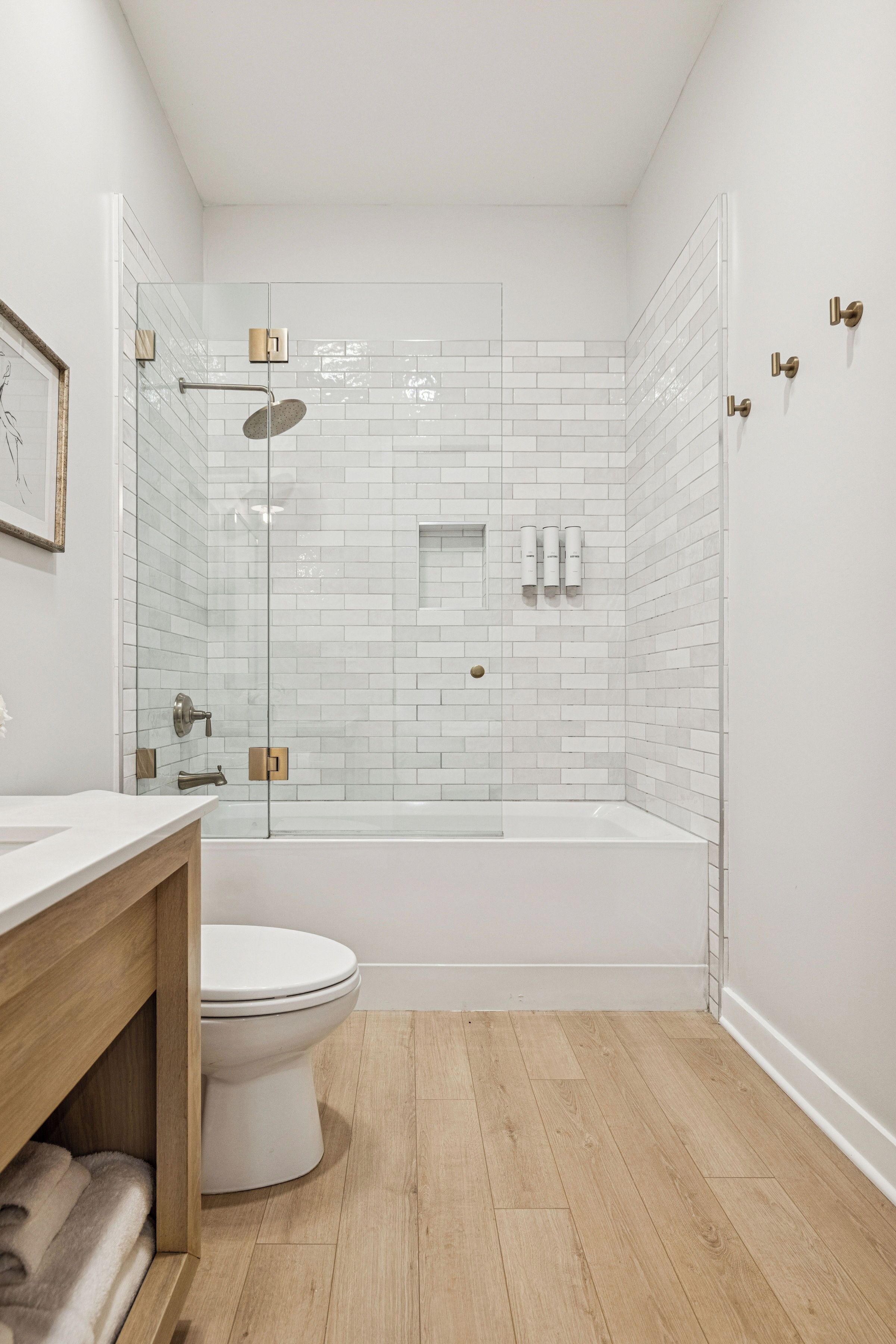 Un baño moderno con ducha envuelta en vidrio, inodoro blanco y tocador de madera.