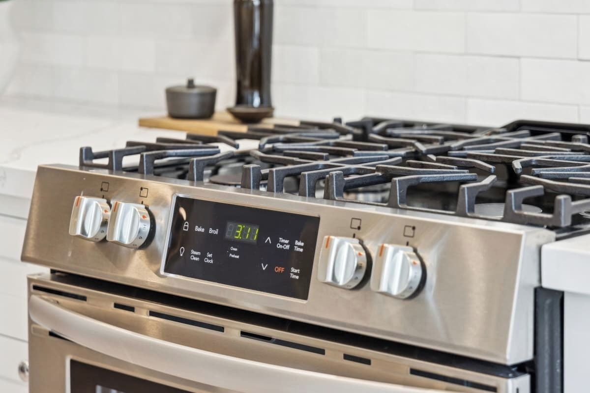 A kitchen with a stainless steel stove and oven, control panel, and a white tiled backsplash.