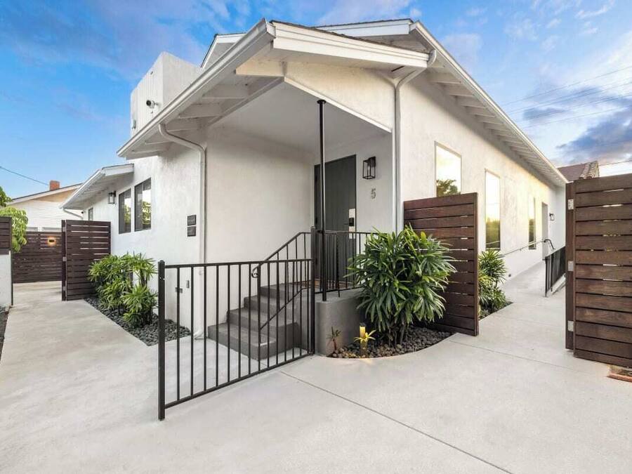 Uma casa moderna de dois andares com varanda coberta, escada e portão.