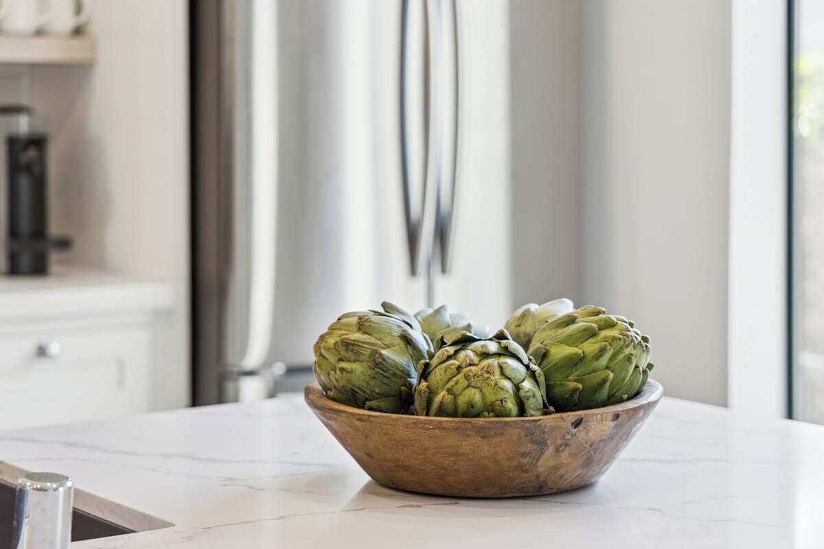 A wooden bowl containing artichokes on a kitchen counter.