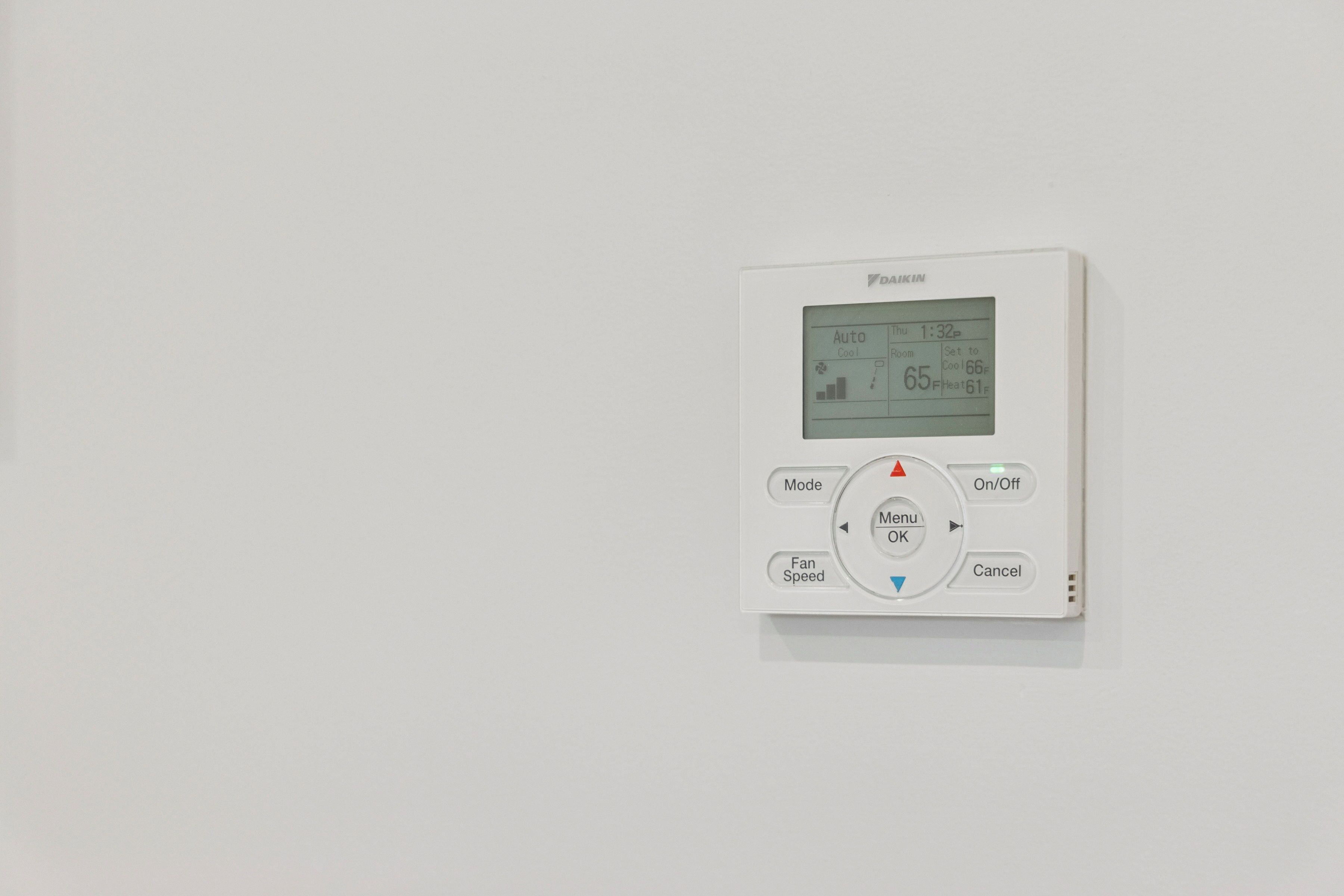 Termostato blanco con pantalla digital, selector de modos y control de velocidad del ventilador.