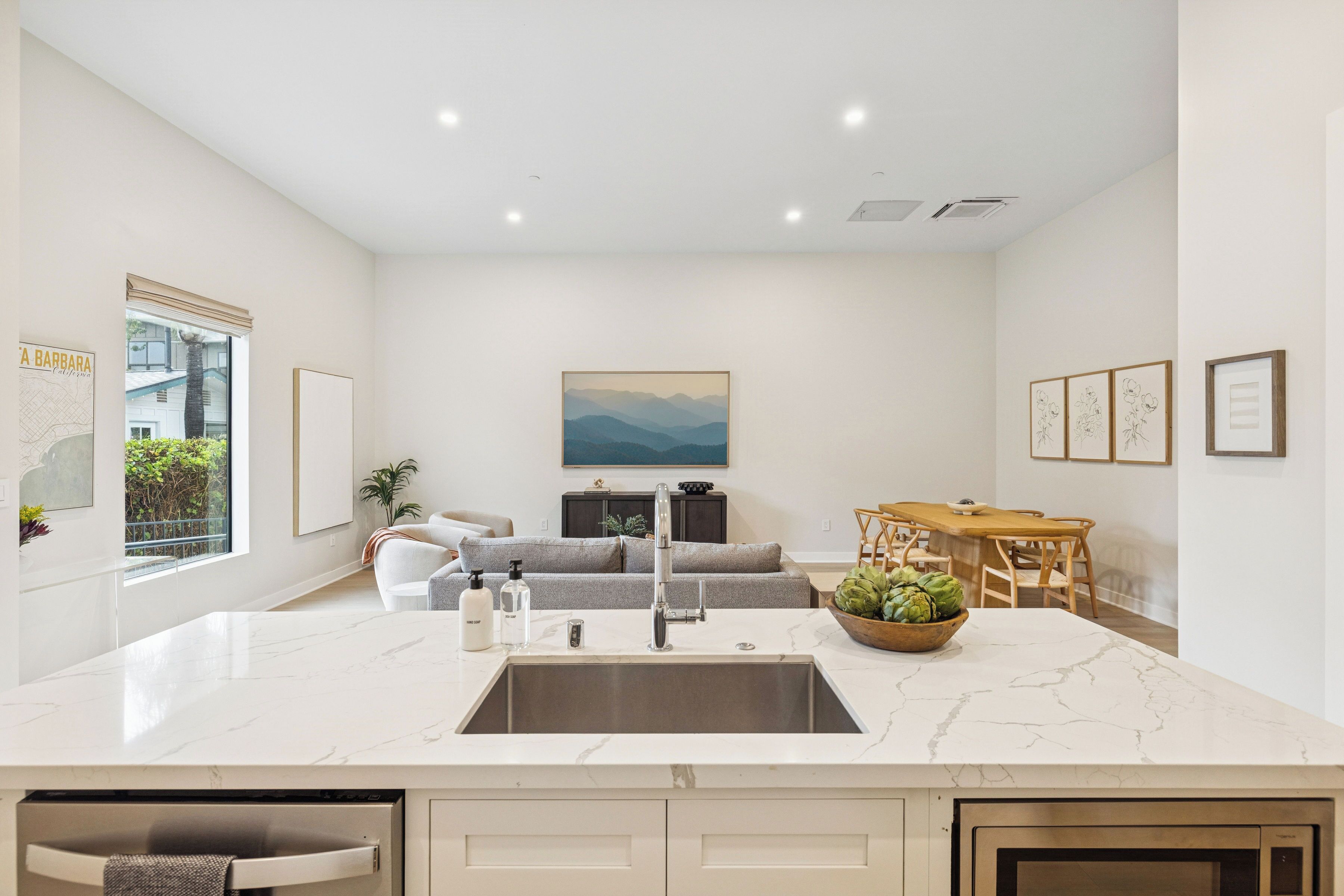 A modern kitchen with a marble countertop, stainless steel sink, and a dining area with a wooden table and chairs.