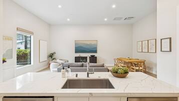 A modern kitchen with a marble countertop, stainless steel sink, and a dining area with a wooden table and chairs.