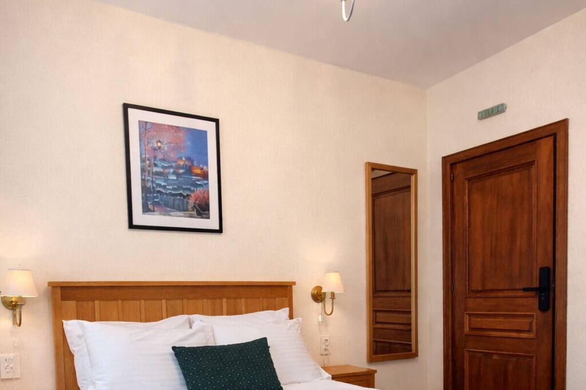 A neatly made bed with a wooden headboard, a green throw blanket, and two bedside lamps.