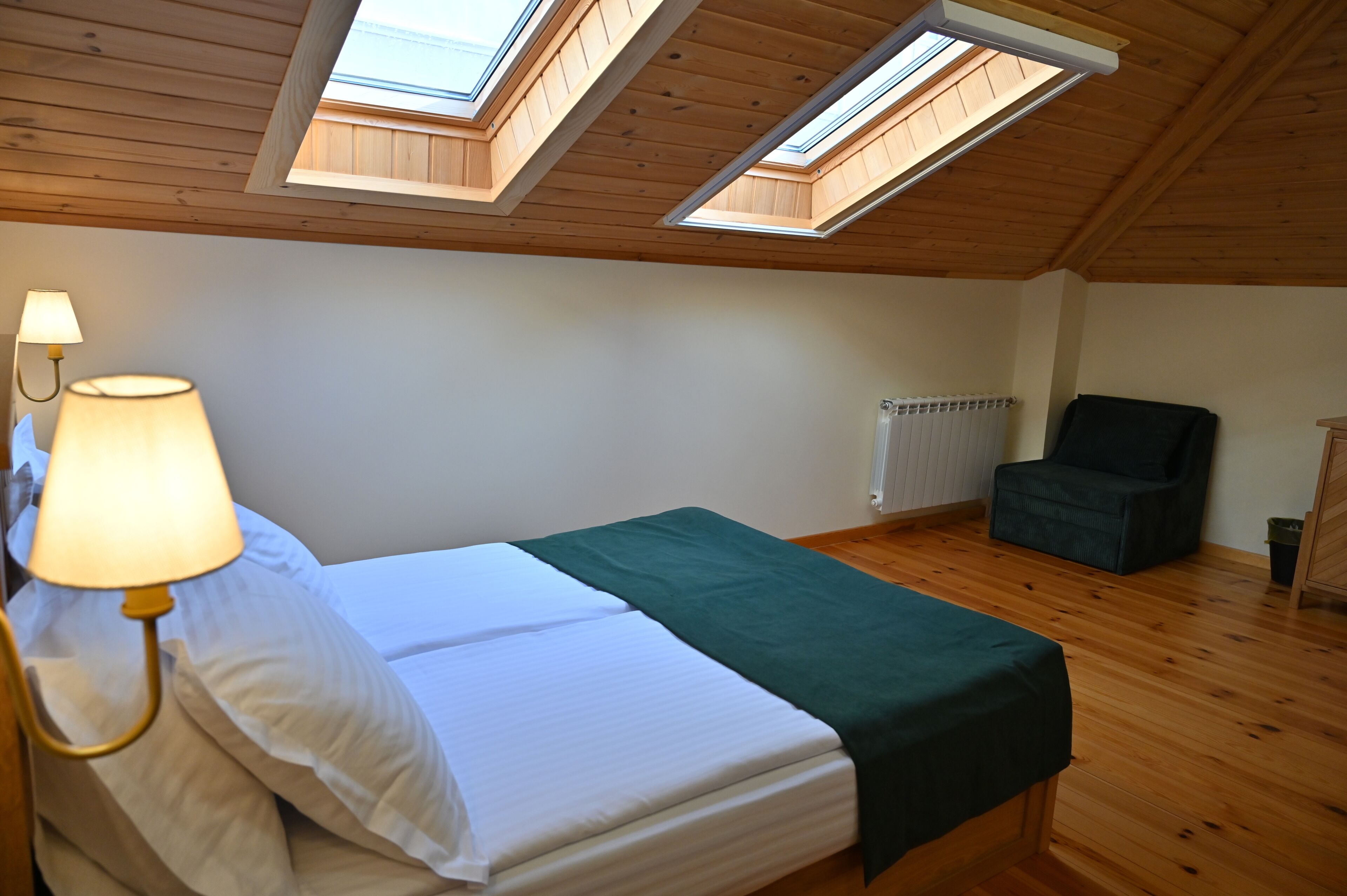 Quarto com cama, poltrona, luminária e claraboias.