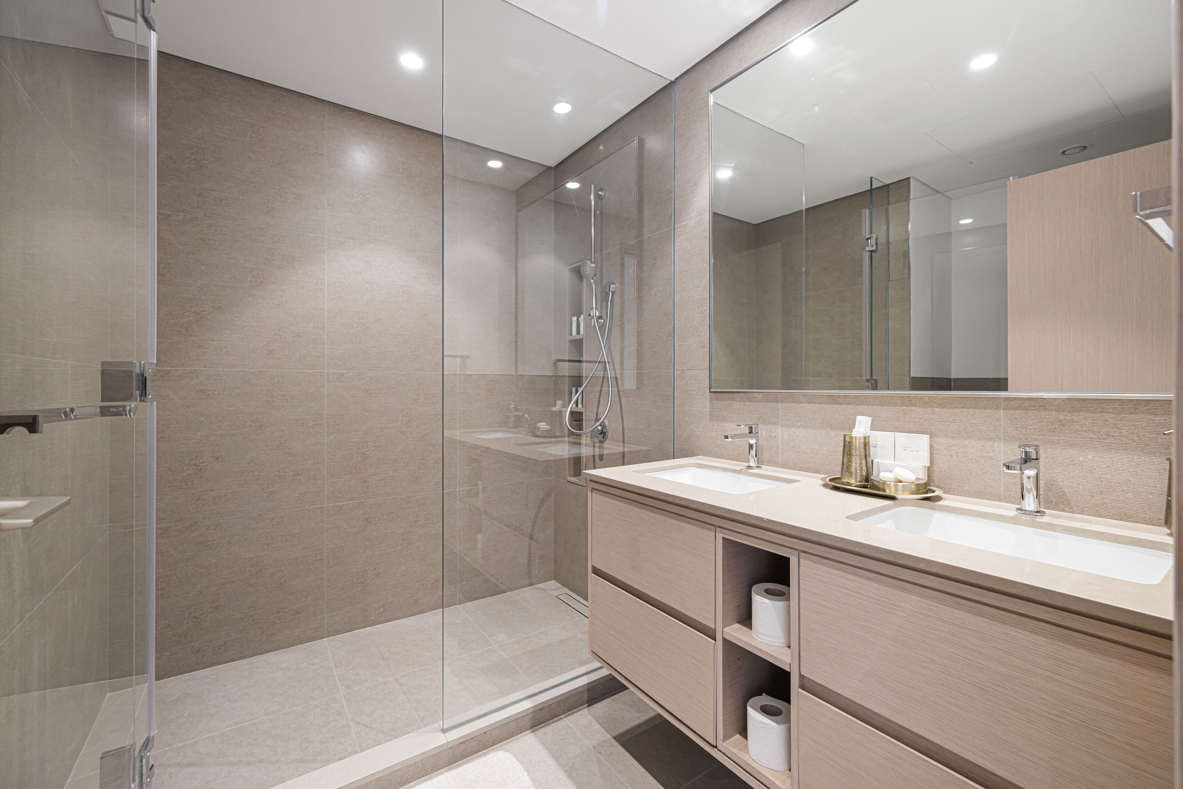 A modern bathroom with a glass-enclosed shower, a large mirror, and a vanity with a sink and storage.