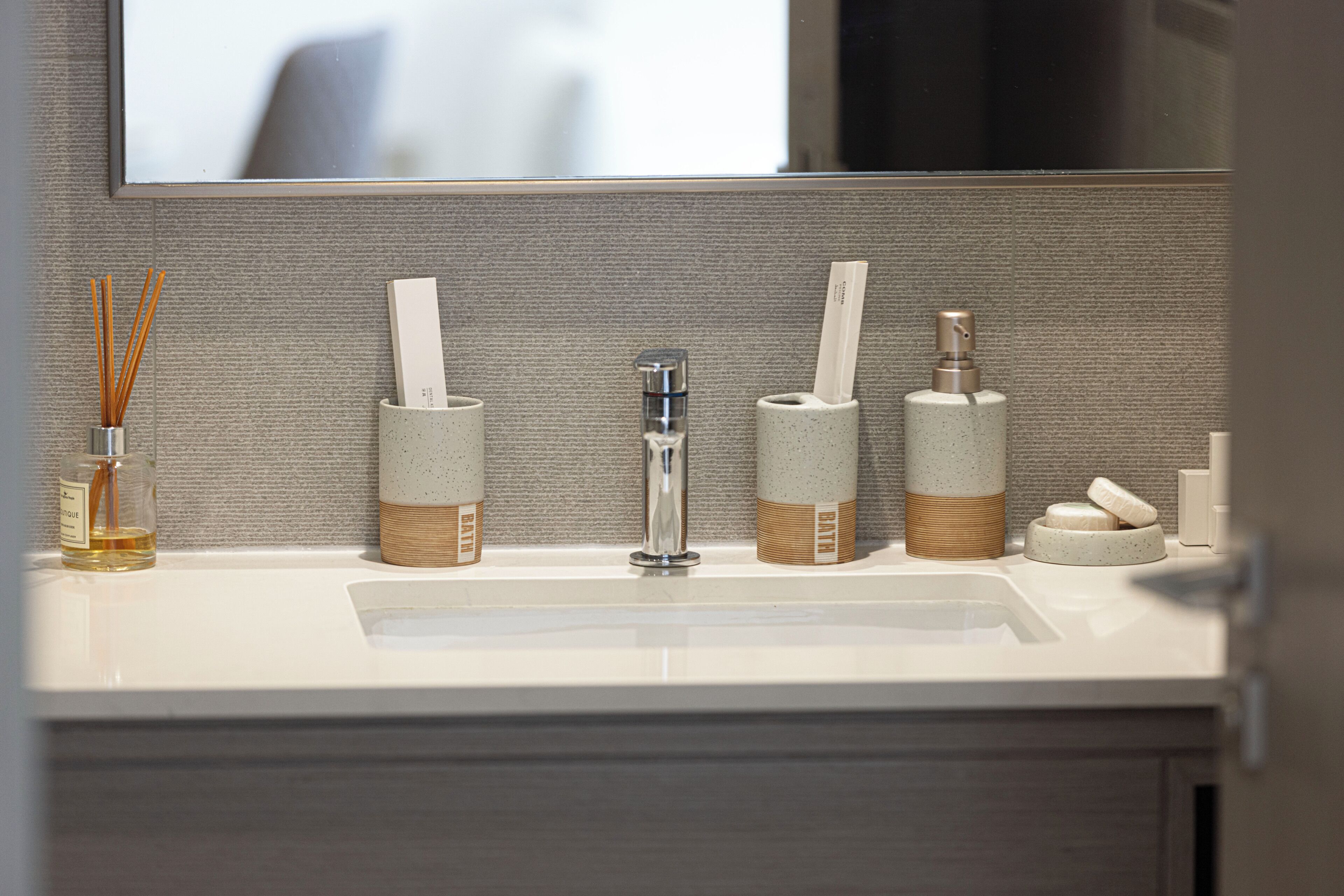 Un meuble-lavabo pour la salle de bain, doté d ’un miroir, d’un évier et d’une rangée de produits de toilette, notamment un distributeur de savon, des supports pour brosses à dents et un flacon de savon liquide.