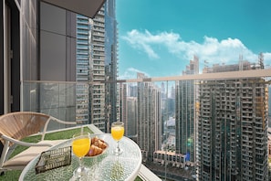 A balcony with a glass table, a wicker chair, and a tray with croissants and orange juice.