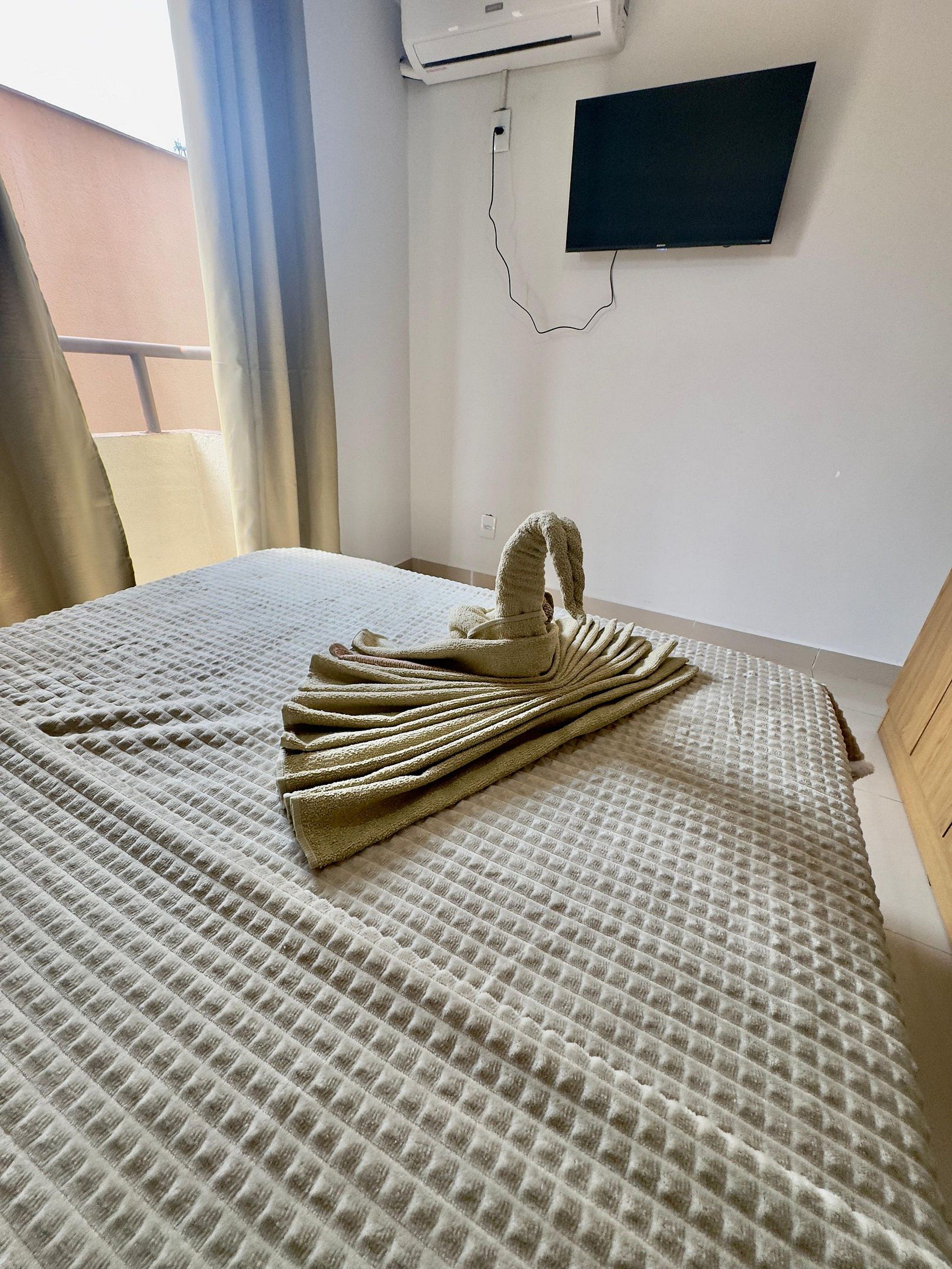 Una habitació d'hotel amb un llit, aire condicionat fixat a la paret i una finestra amb cortines.