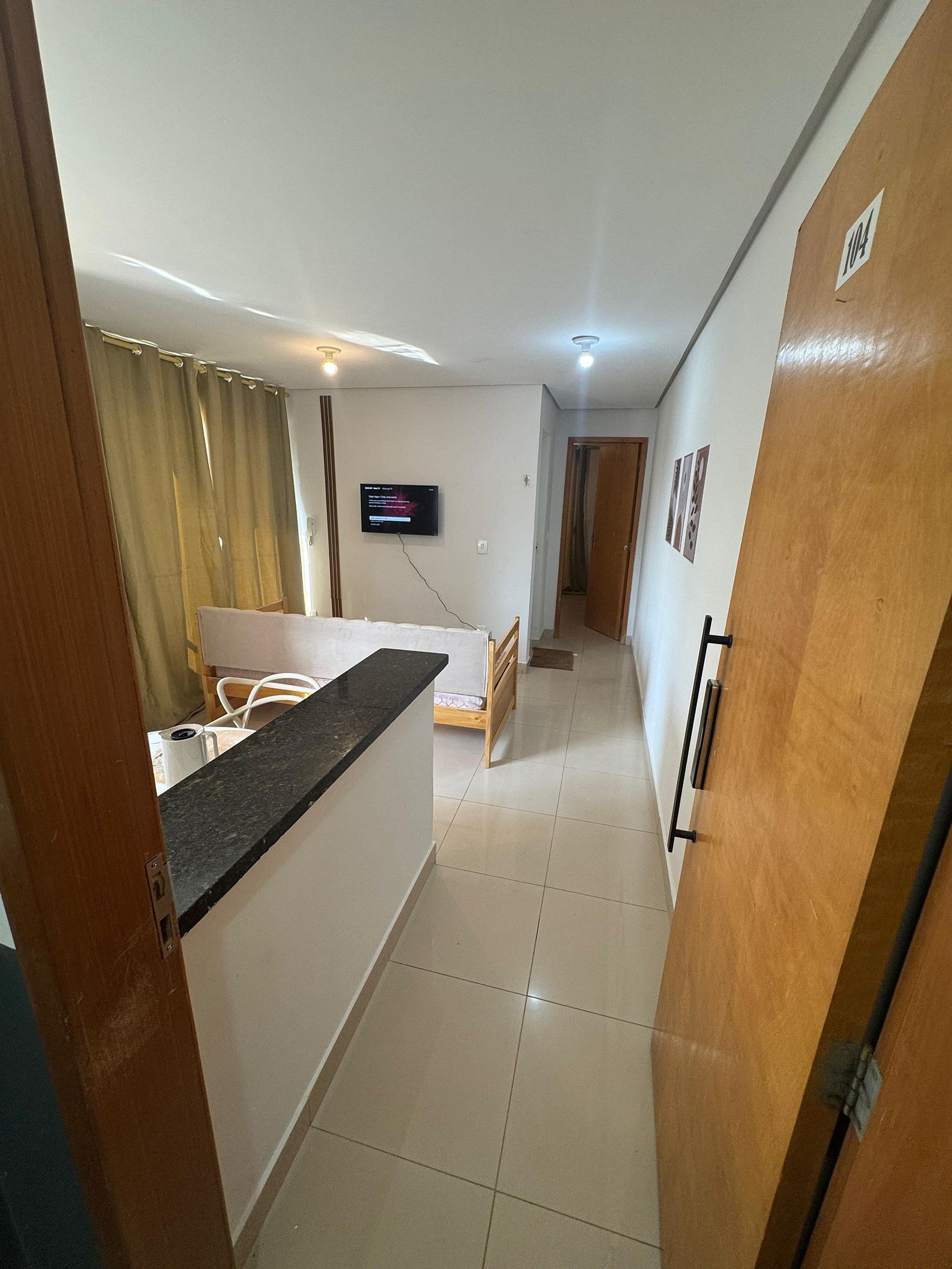 A compact living space with a kitchenette, a bed, a TV, and a door with a number.