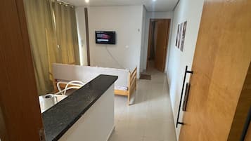 A compact living space with a kitchenette, a bed, a TV, and a door with a number.