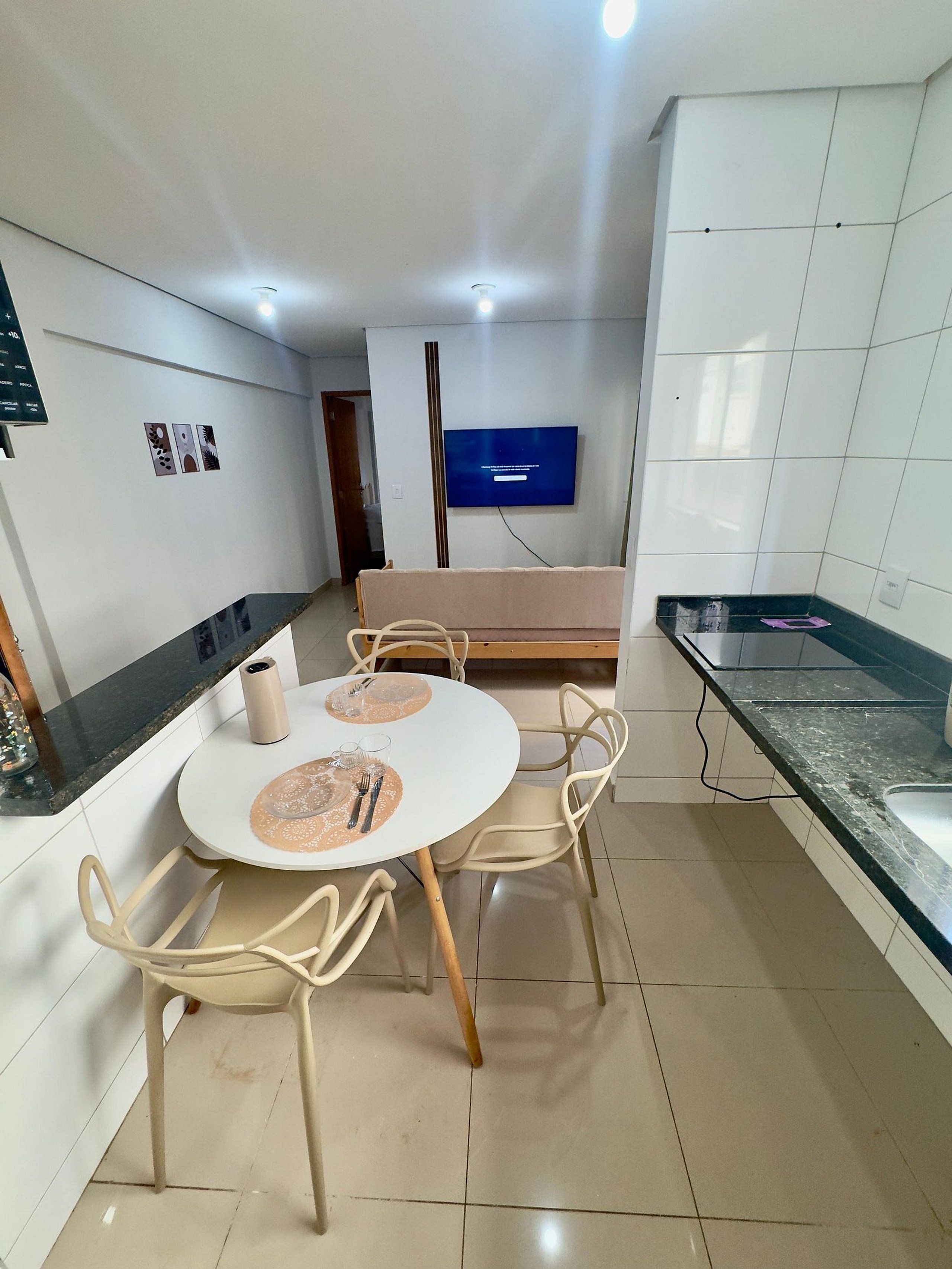 Una cocina moderna con armarios blancos, una mesa de comedor con sillas y un televisor de pantalla plana montado en la pared.