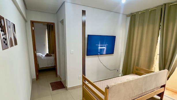 A bedroom with a bed, a television, and a bathroom visible through an open door. - Residencial Gomes (Goiânia)
