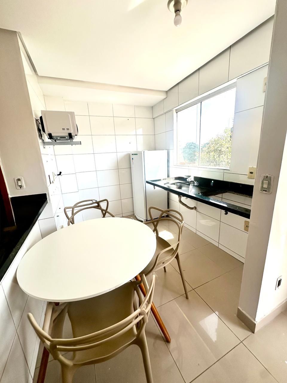 Cozinha moderna com mesa redonda e cadeiras, geladeira e janela que proporciona luz natural.