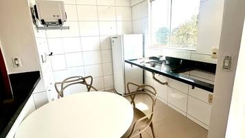 Cozinha moderna com mesa redonda e cadeiras, geladeira e janela que proporciona luz natural.
