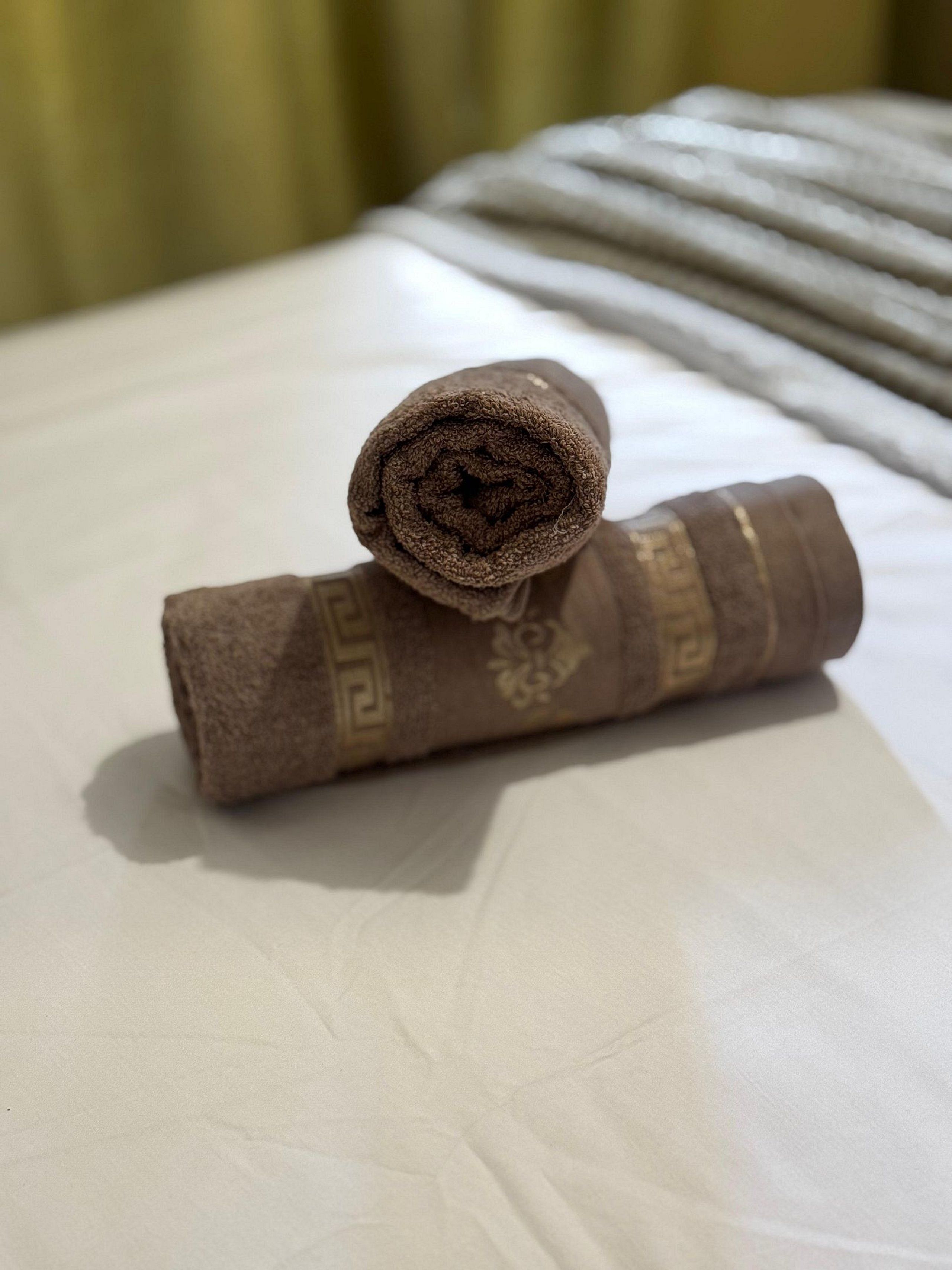 A rolled towel with a patterned design on a bed.