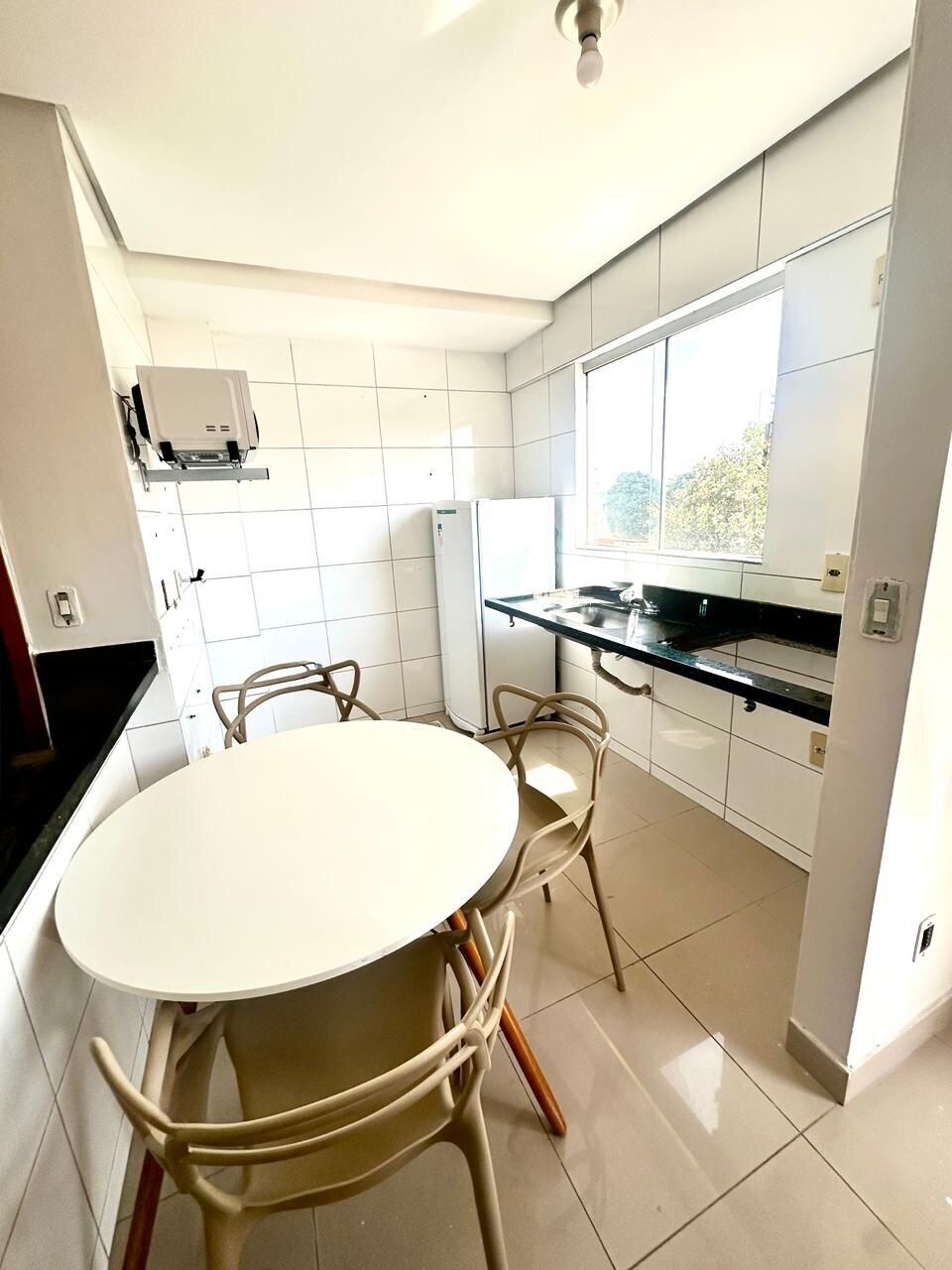 Una cocina moderna con una mesa redonda y sillas, un refrigerador y un ventanal que proporciona luz natural.