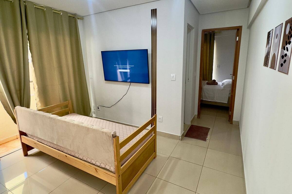 A bedroom with a wooden bed, a TV mounted on the wall, and a ceiling light.