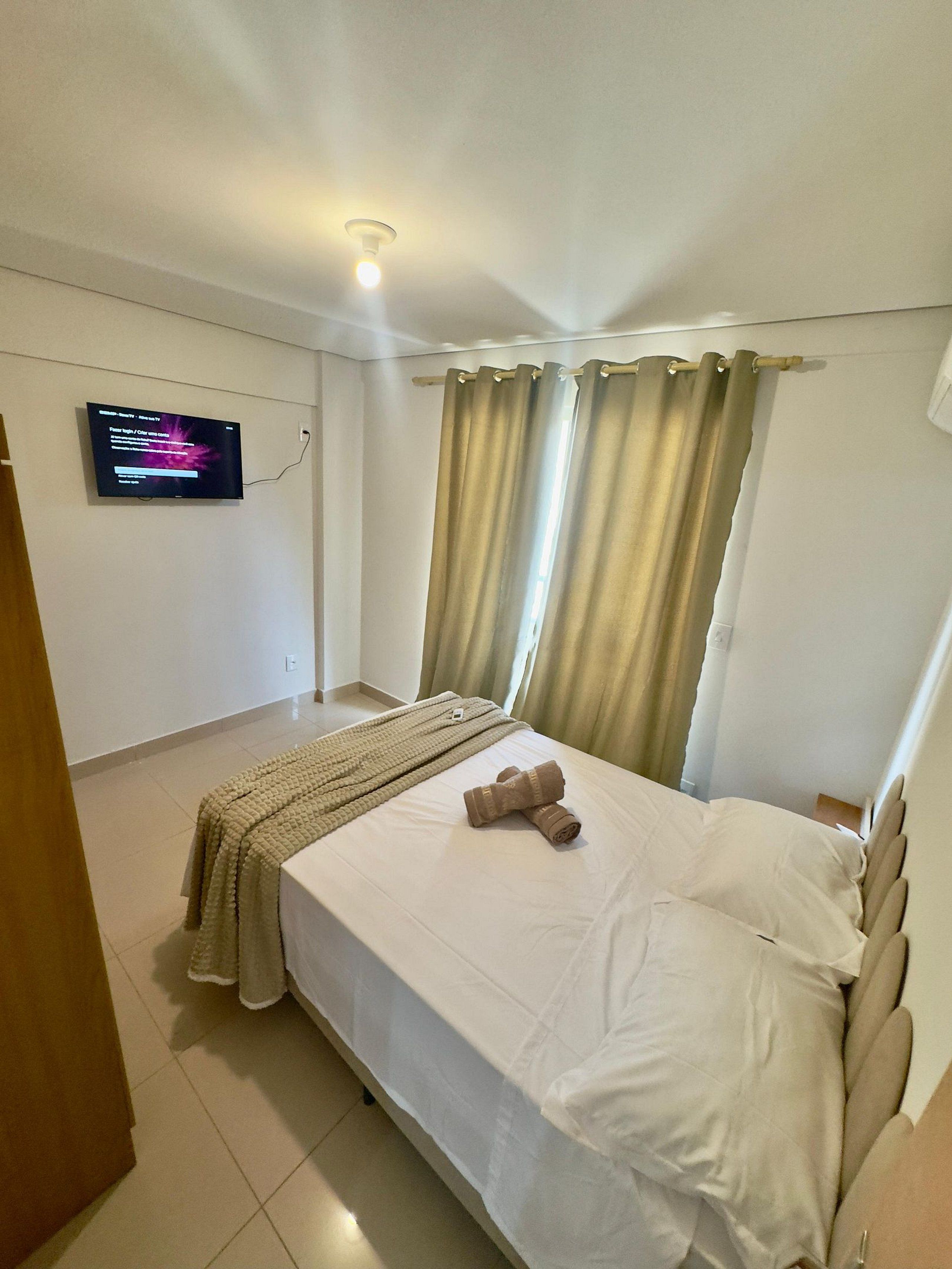 Una camera d'albergo con un letto, una TV fissata al muro e tende alle finestre.