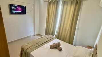 Una camera d'albergo con un letto, una TV fissata al muro e tende alle finestre.
